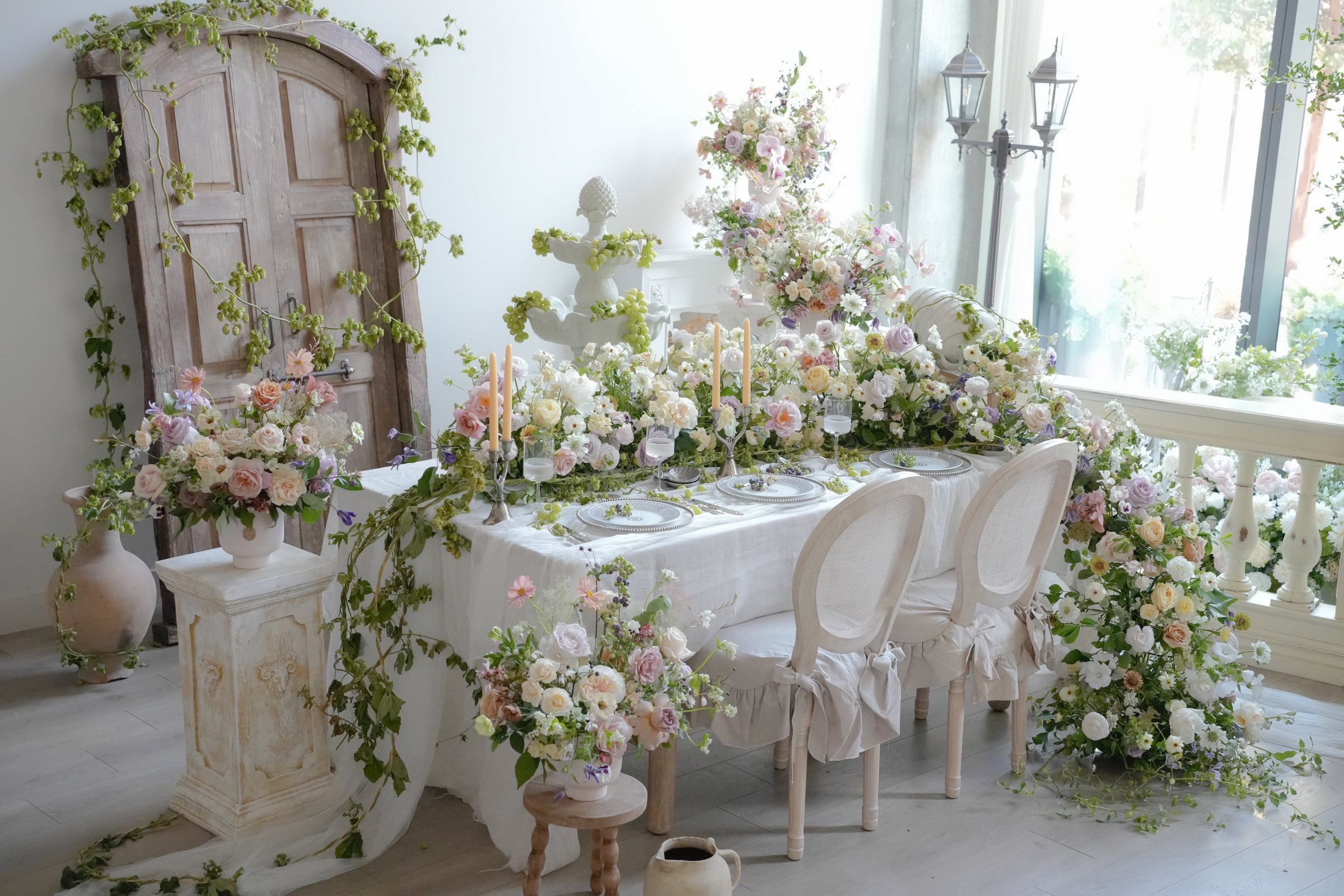 A pastel wedding tablescape with trailing greenery, an antique door backdrop and slipcovered chairs