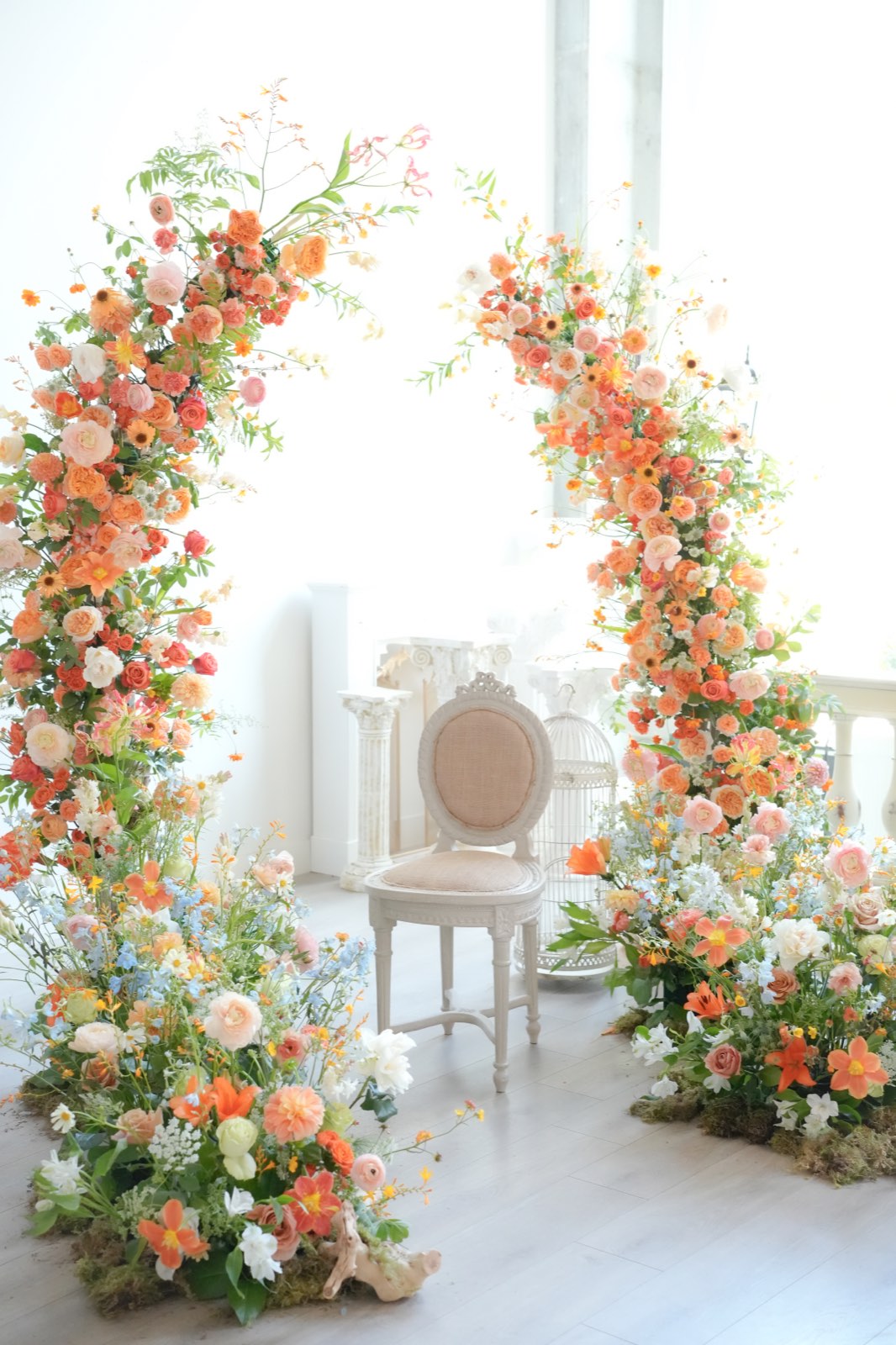 Peach and coral ceremony arch with a soft chair beneath, in a bright white room